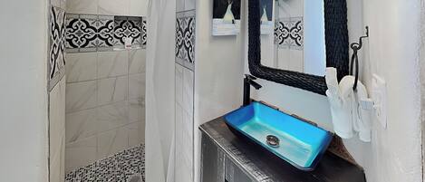 Une salle de bain avec une douche, un lavabo bleu et un miroir.