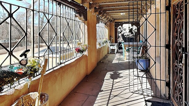 Un pasillo con ventanas con barrotes, suelo de baldosas y una puerta con detalles de metalería.