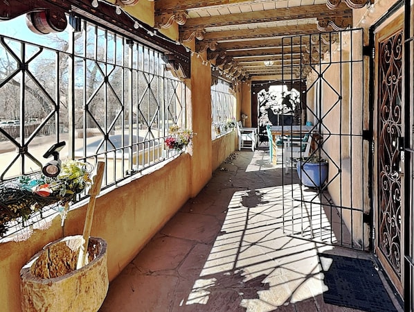 Un couloir avec des fenêtres grillagées, un sol carrelé et une porte ornée de motifs en métal.