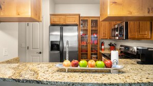 Une cuisine dotée de plans de travail en granit, de meubles en bois, d’appareils électroménagers en acier inoxydable et d’un présentoir à fruits.