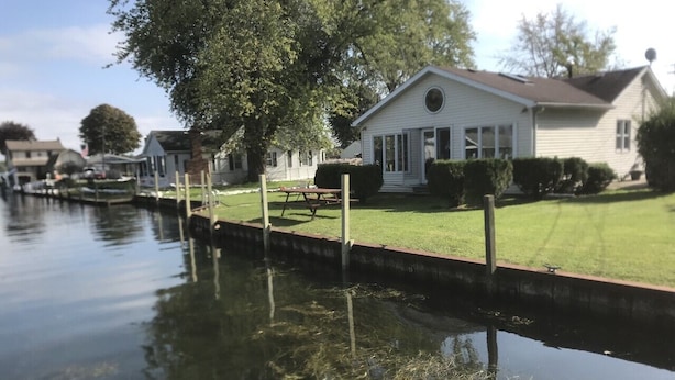 A canal with a house on the right, a grassy area, and a dock. - Cheerful 3 bedroom cottage with River access. (Clay Township)