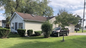 A single-story house with a front porch, a lawn, and a parked SUV. - Cheerful 3 bedroom cottage with River access. (Clay Township)