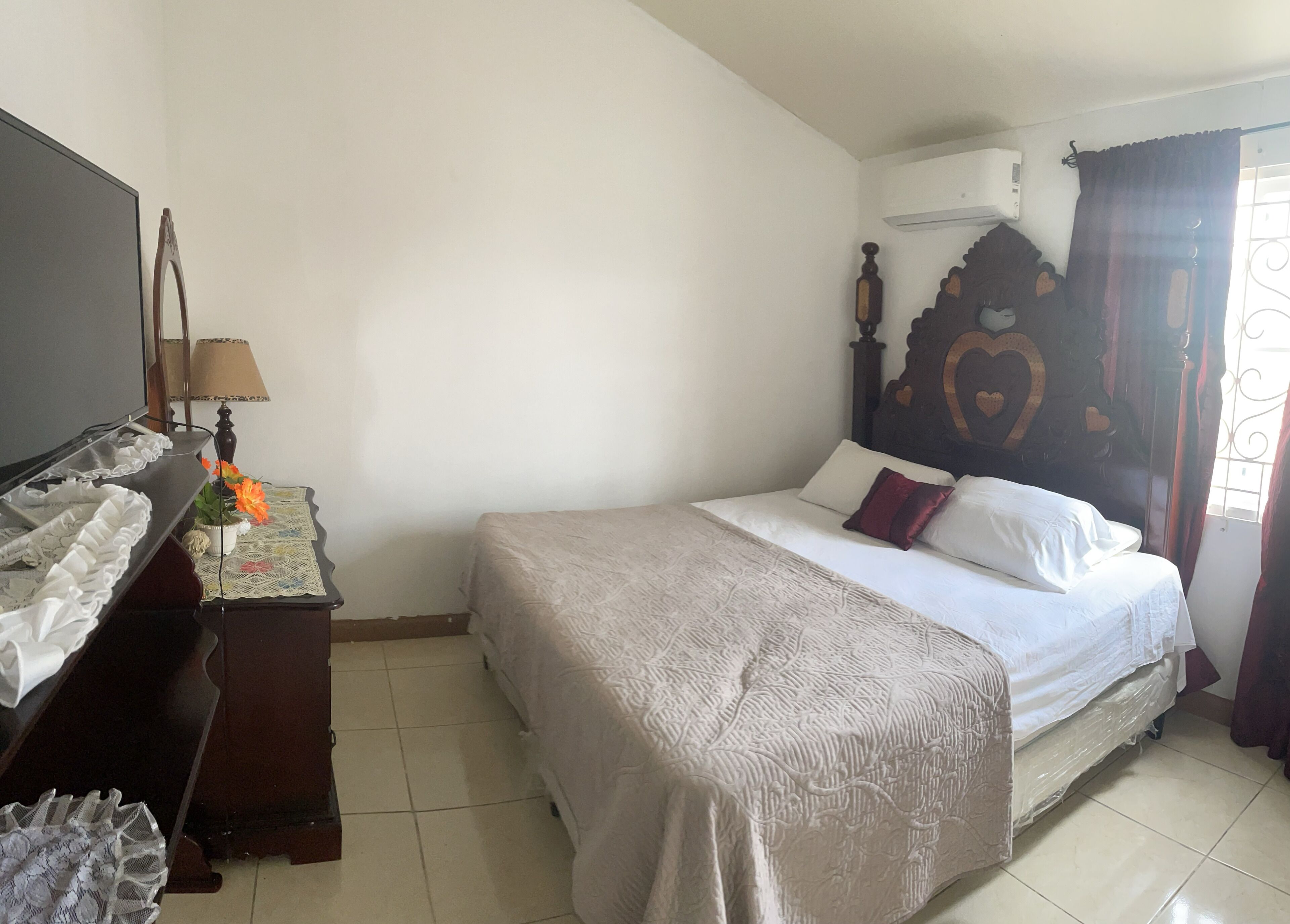 A bedroom with a bed, a dresser, a lamp, and a window with curtains.