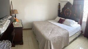 A bedroom with a bed, a dresser, a lamp, and a window with curtains. - Spacious 9 BED family sized house in a gated community (Trelawny Parish)