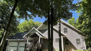 A two-story house with a front porch, garage, and a large tree in front.