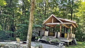 A wooden gazebo in a forested area with a stone pathway leading to it.