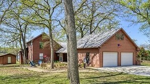 A two-story wooden house with a garage, surrounded by trees and a well-maintained lawn. - A Dream Come True Lake House  - The prettiest sunset view on the lake! (Marquez)