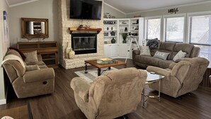 A living room with a stone fireplace, a ceiling fan, and a television. There are two sofas and a coffee table. - A Dream Come True Lake House  - The prettiest sunset view on the lake! (Marquez)