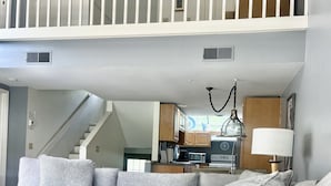 Ein Wohnzimmer mit einem grauen Ecksofa, einem Holztisch und einer Treppe, die zu einer oberen Ebene führt.