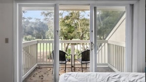 Ein Schlafzimmer mit einer Schiebetür zu einem Balkon mit weißer Geländer und zwei schwarzen Stühlen.