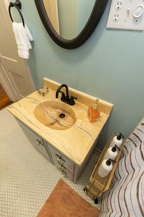 Ein Badezimmer mit einem beige-marmornen Waschbecken, einem schwarzen Wasserhahn, einem Seifenspender und einem Handtuchhalter mit weißen Handtüchern.