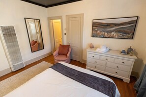 Ein Schlafzimmer mit einem Bett, einem Schminktisch, einem Sessel und einem Bild an der Wand.