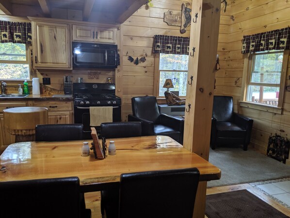 A wooden cabin interior with a kitchen, dining area, and two black leather chairs.