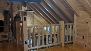 A wooden cabin interior with a TV mounted on the ceiling, a wooden table with a decorative item, and a staircase leading to an upper level.