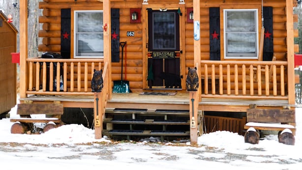 A wooden cabin with a front porch, a star on the roof, and a 'Welcome' sign.