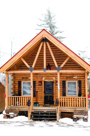 A wooden cabin with a front porch, a star on the roof, and a 'Welcome' sign.