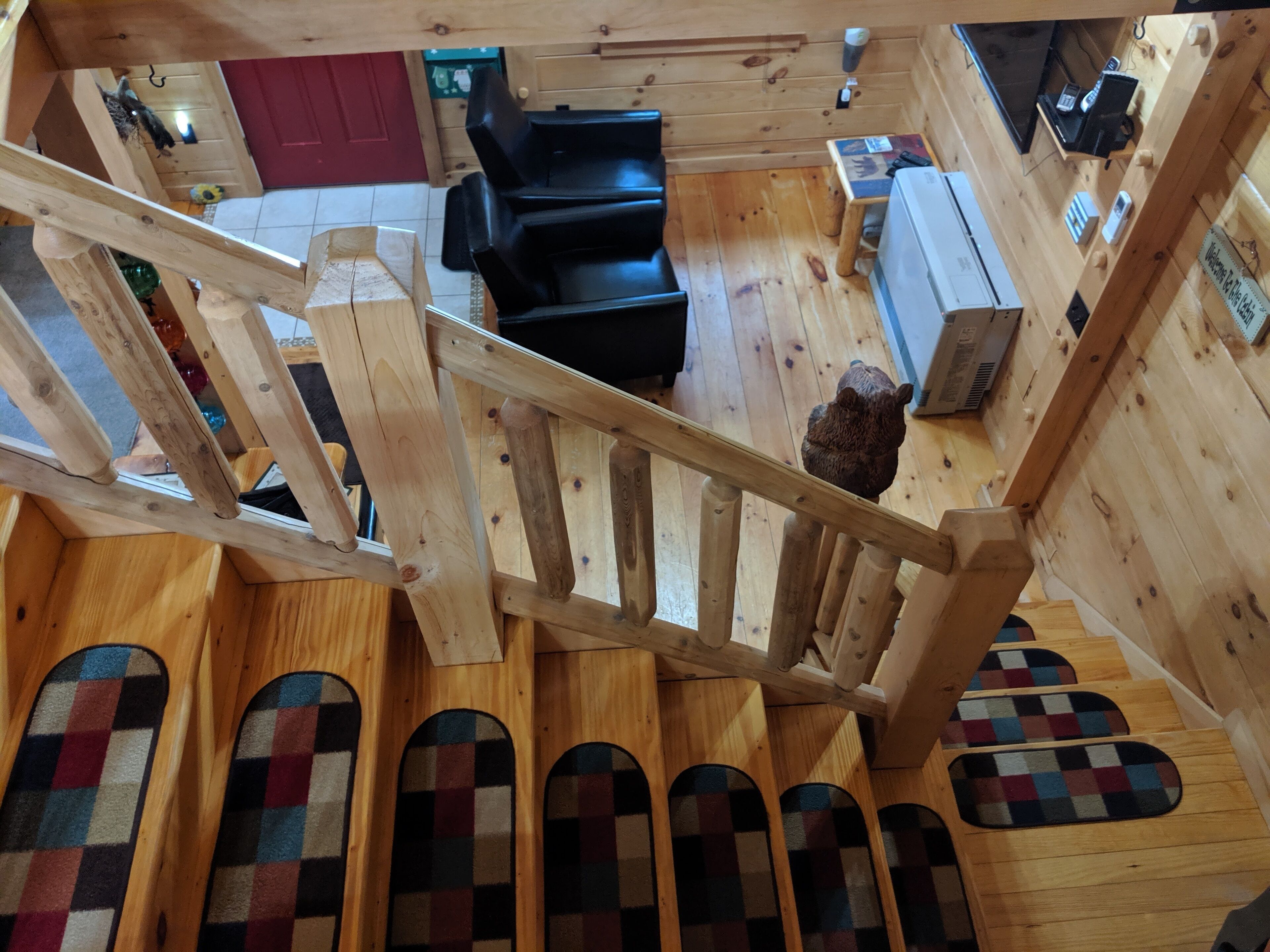 Un intérieur en bois avec un escalier, un canapé noir, une petite table et un ours en peluche.