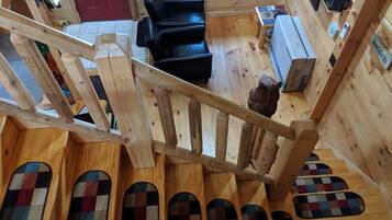 Un intérieur en bois avec un escalier, un canapé noir, une petite table et un ours en peluche.