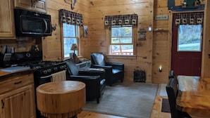 A cozy cabin interior with wooden walls, a kitchen with a stove and microwave, a dining table, and a fireplace.