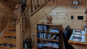 A wooden cabin interior with a staircase, bookshelves, and a dining area.