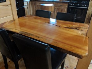 Ein Holztisch mit vier Stühlen, eine Küche mit Holzschränken und einem Herd im Hintergrund.