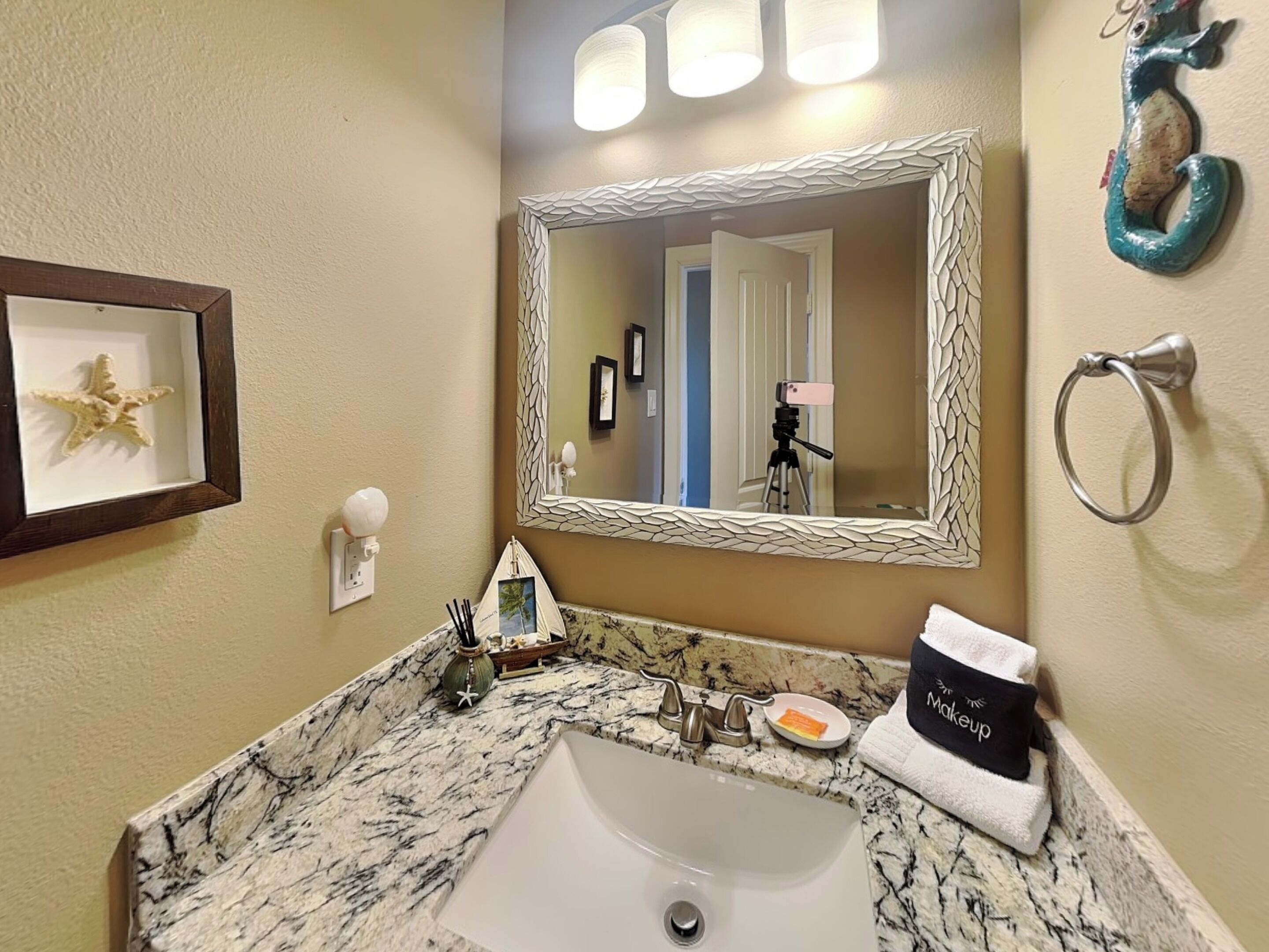 A bathroom with a marble sink, a framed seastar decoration, a mirror with a textured frame, and a towel rack with a towel.