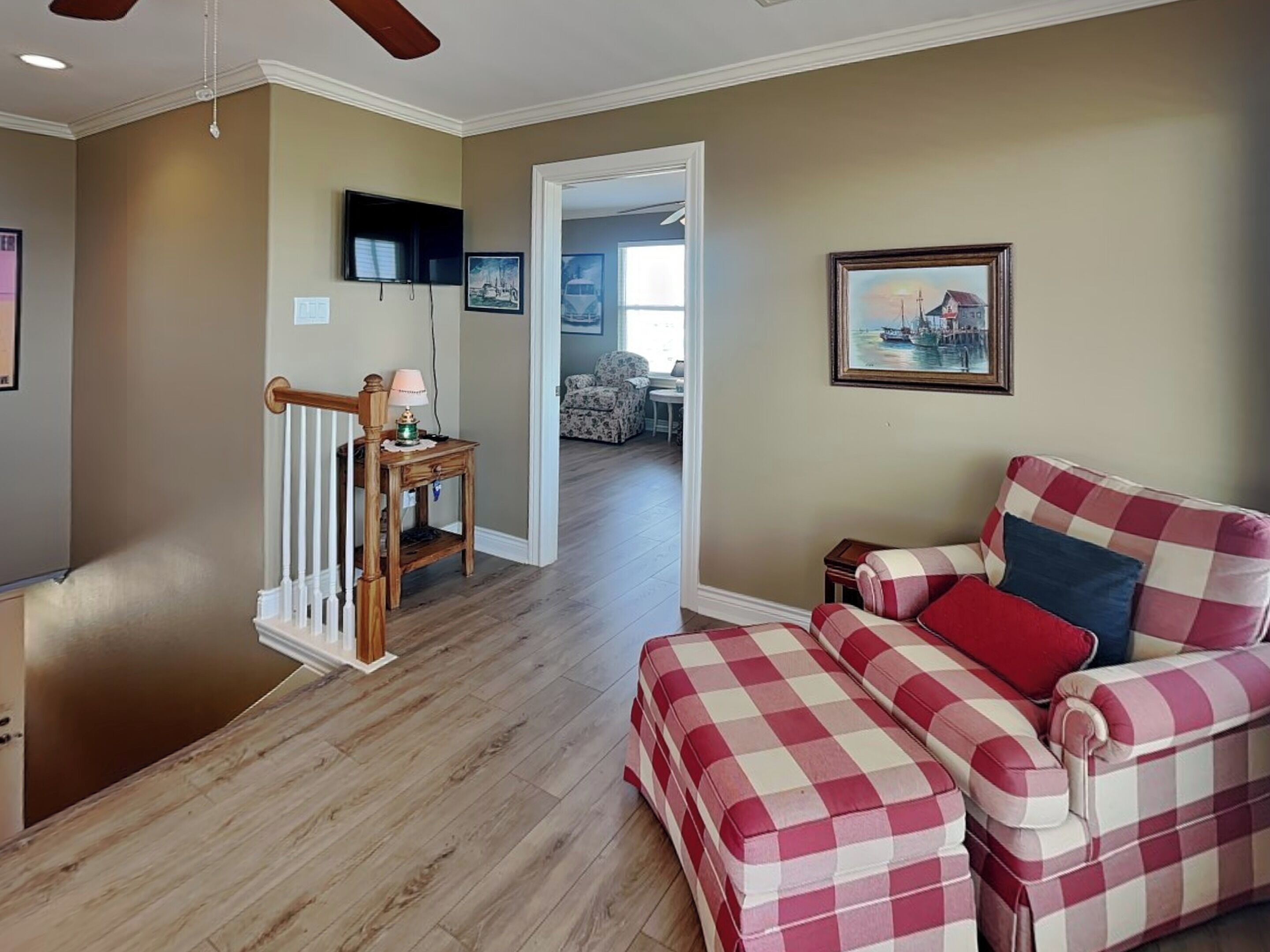 A living room with a checkered sofa, a television, a painting, and a staircase.