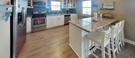 A kitchen with white cabinets, a granite countertop, and a central island with bar stools.
