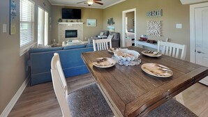Een eetgedeelte met een houten tafel, witte stoelen en een blauwe bank op de achtergrond.