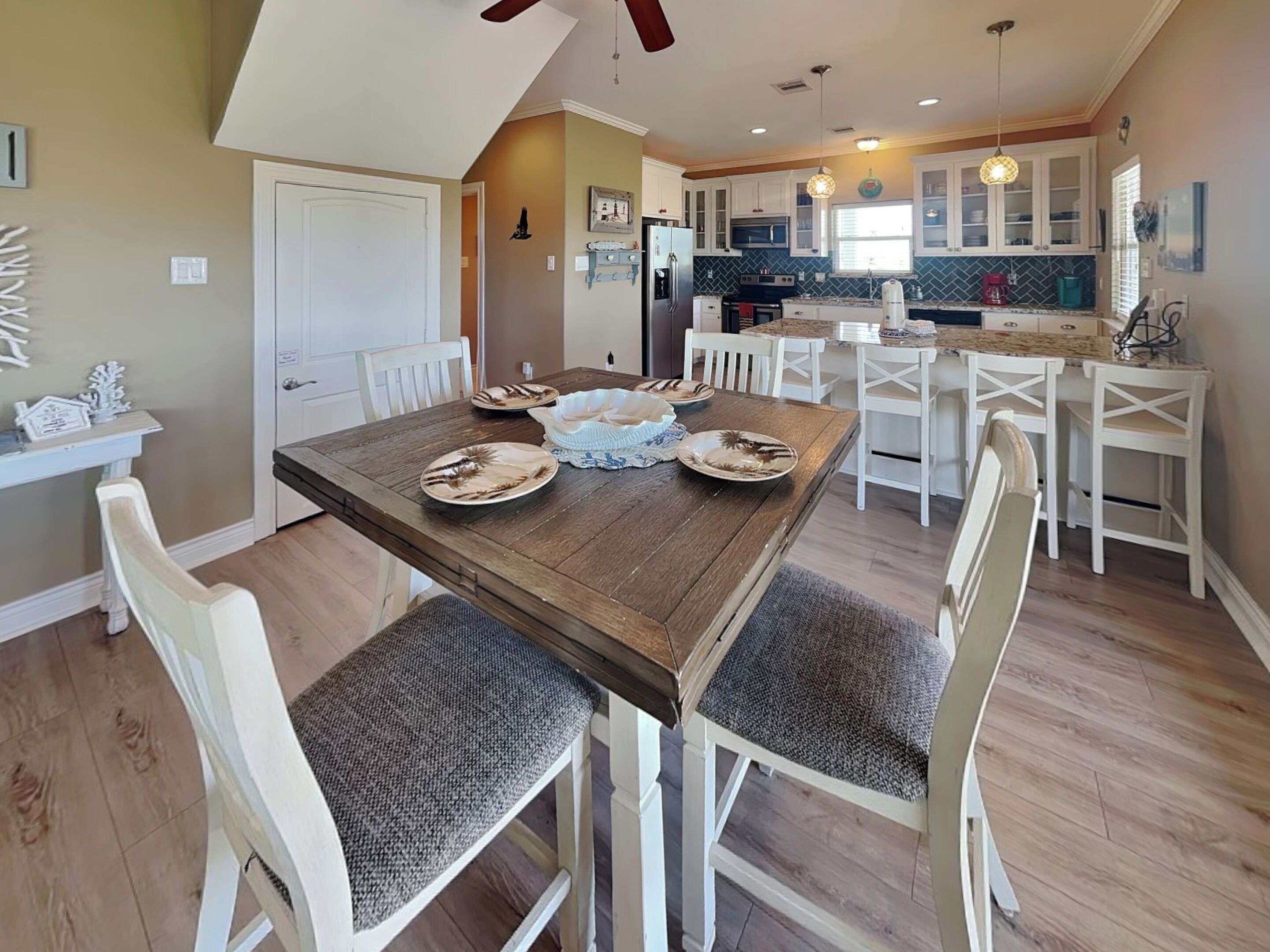 A dining area with a wooden table, white chairs, and a kitchen in the background.