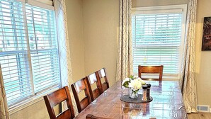 A dining room with a wooden table and chairs, a vase with flowers, and a window with blinds. - Aspen Villa-Country Club, Augustana, USF & Sanford Med. (Sioux Falls)