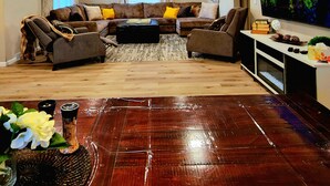 A living room with a large flat-screen TV, a sofa set, a coffee table, and a wooden dining table with a vase of flowers. - Aspen Villa-Country Club, Augustana, USF & Sanford Med. (Sioux Falls)