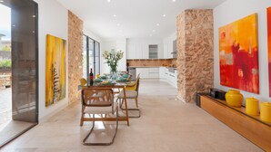 A modern kitchen with white cabinets, a stone accent wall, and a dining area with a glass table and chairs. - CAN FONT (COSTITX) - Stunning villa with private pool and free WiFi. (Costitx)
