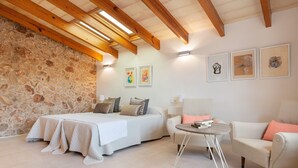 A bedroom with a stone wall, a bed, a sofa, a small table, and three framed artworks on the wall. - CAN FONT (COSTITX) - Stunning villa with private pool and free WiFi. (Costitx)