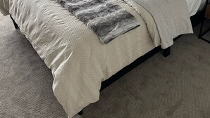 Ein Schlafzimmer mit Bett, Fenster, Wandbehang aus Makramee und Nachttisch.