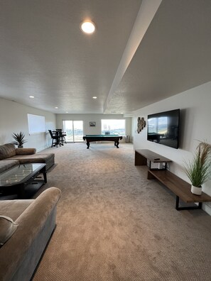 A spacious living room with a pool table, a sofa, a coffee table, and a TV mounted on the wall. - Newly Built Mountain Escape - Modern Home (Eden)