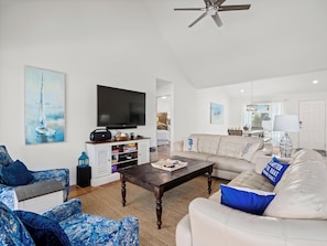A spacious living room with a flat-screen TV, a sofa, a coffee table, and a ceiling fan.