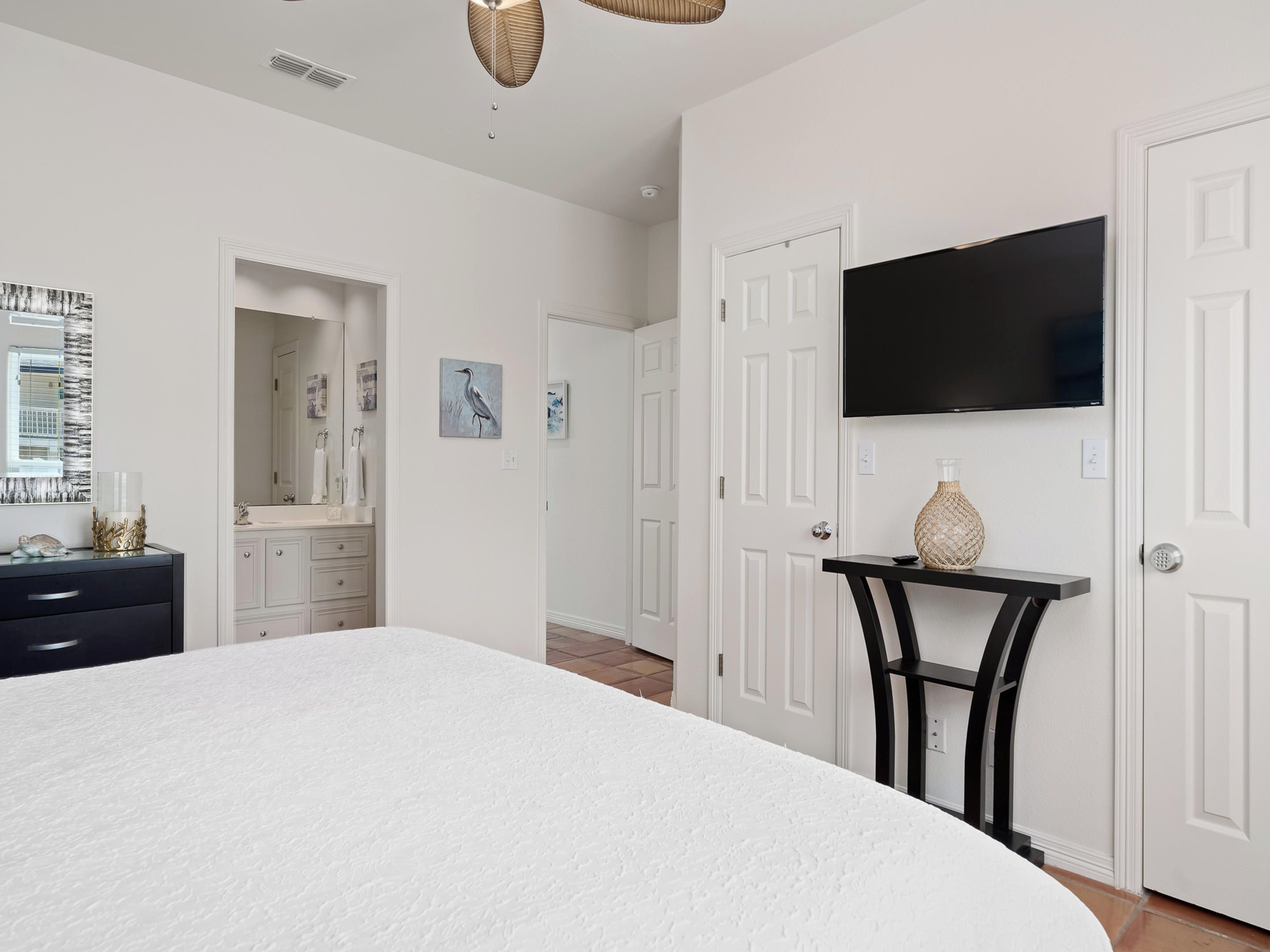 Quarto com cama grande, cômoda, penteadeira, espelho, televisão e porta que dá para outro espaço.