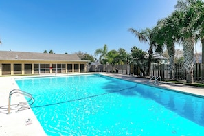 Una piscina rectangular con agua cristalina y azul, rodeada por una valla de madera y palmeras.