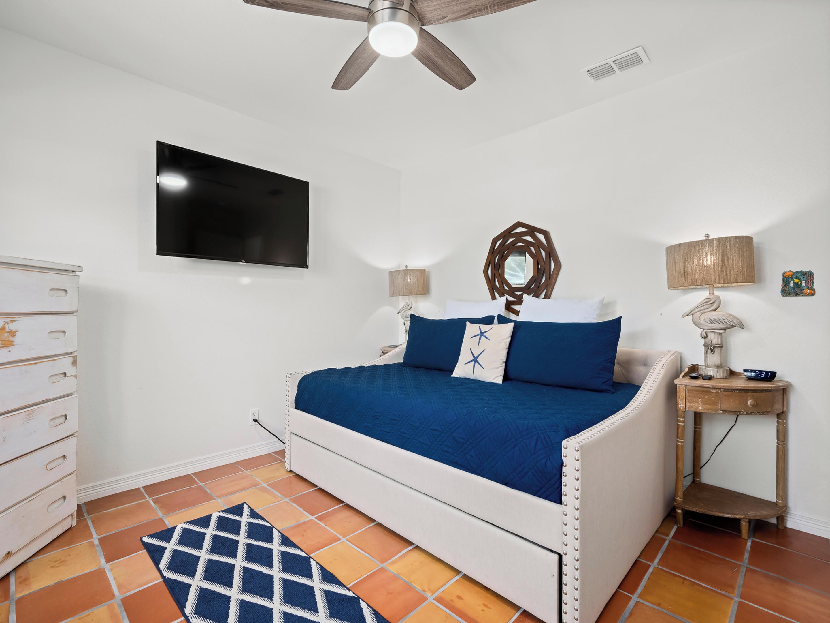 Un dormitorio con cama, televisión, ventilador de techo, mesita de noche y cómoda.