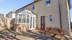 A residential building with a conservatory, a wooden bench, and a paved courtyard. - St Marys Cottages No1 (Alnwick)