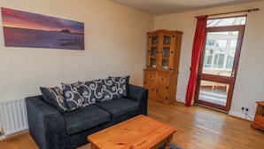 A living room with a sofa, a wooden coffee table, a cabinet, and a painting on the wall. - St Marys Cottages No1 (Alnwick)