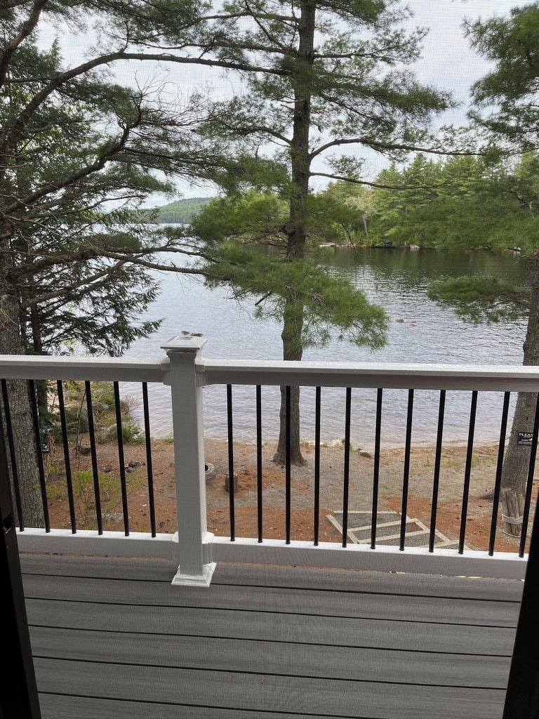 A wooden deck with a white balustrade overlooking a lake with trees.