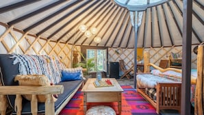 A cozy interior of a yurt with a sofa, a bed, a small table, and a wooden stool.
