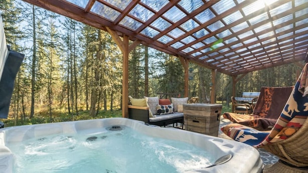 A hot tub in a covered outdoor area with a wooden pergola, surrounded by forest.