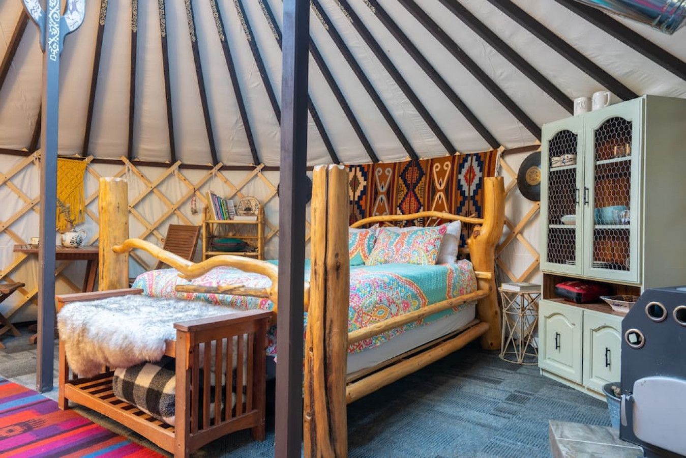 Una tienda acogedora y bien amueblada con una cama de madera, una pequeña mesa de madera y un mueble con diseño de panal.