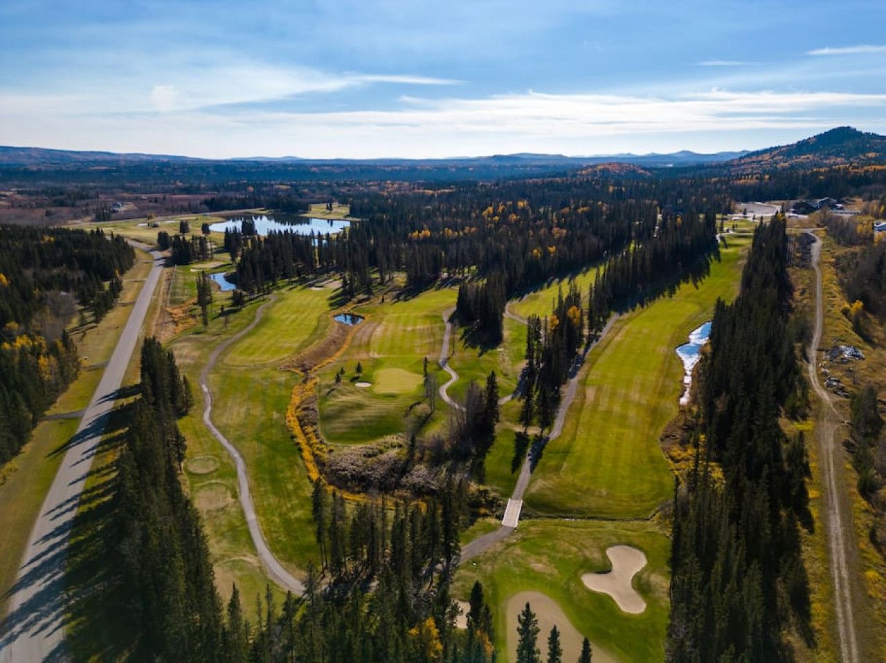 An aerial view of a golf course with multiple holes, surrounded by dense forests and a lake.