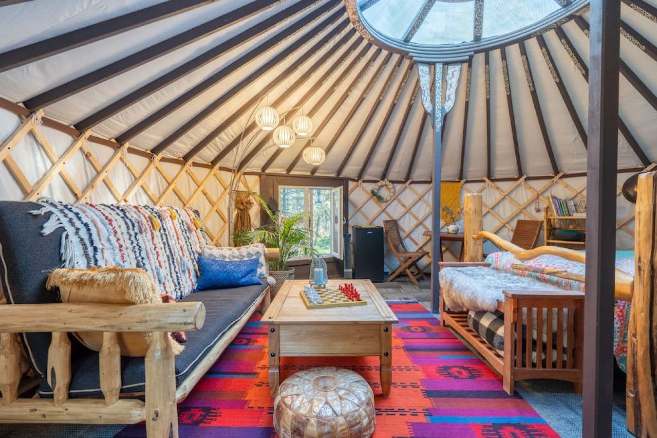 A cozy interior of a yurt with a sofa, a bed, a small table, and a wooden stool.