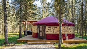 A yurt with a wooden platform and a door, surrounded by trees in a forest setting.