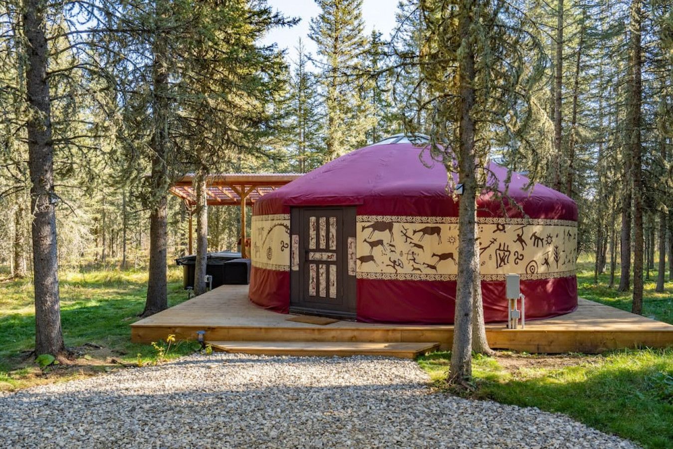 Una yurta con una piattaforma di legno e una porta, circondata da alberi in un bosco.